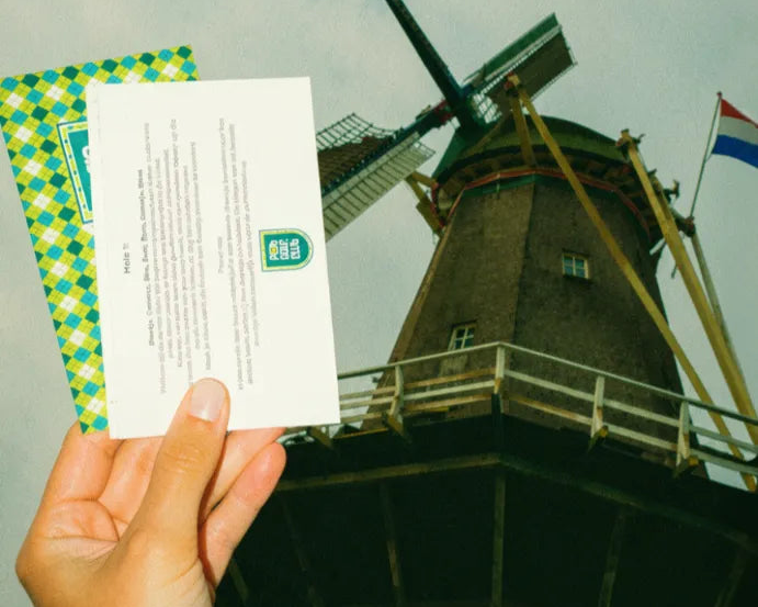 Hand holding printed pub golf scorecards in front of a Dutch windmill