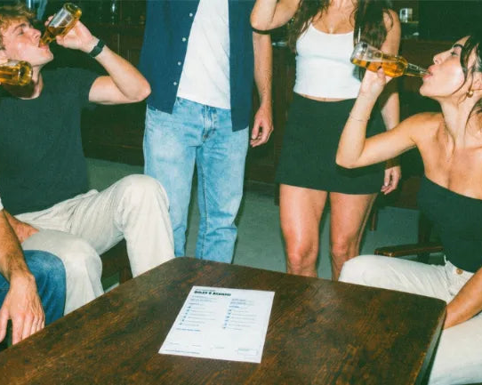 Four friends taking a drink together around a pub table with their pub golf scorecard on it
