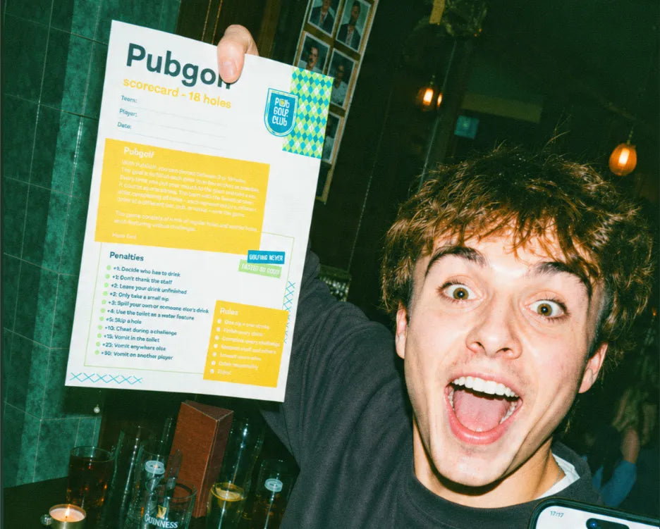 Player grinning as he holds up his 18 hole printable pub golf scorecard in a pub
