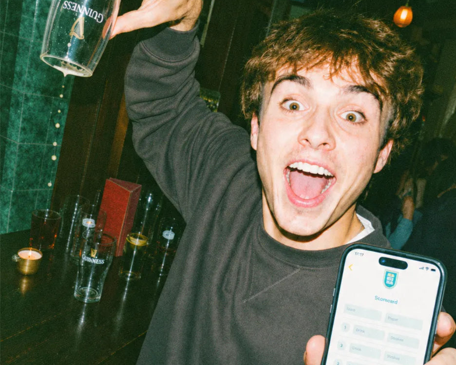 Player raising an empty glass and showing his live pub golf scorecard on his phone