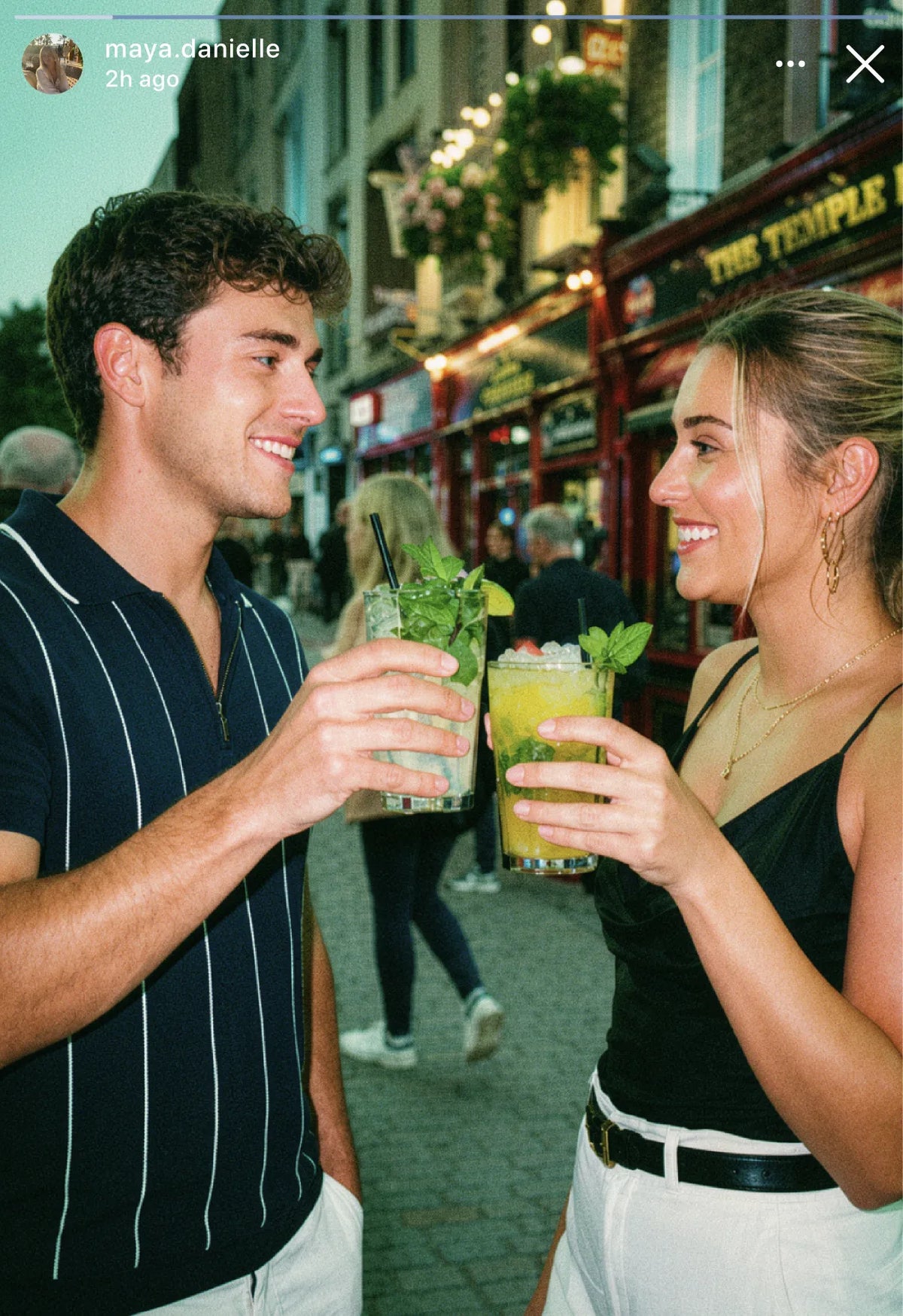 Instagram story of two friends clinking tall cocktails on a busy pub street in the evening
