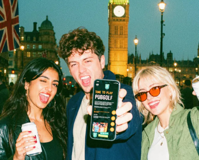 Three friends holding up a phone with the Pub Golf Club app in front of Big Ben at night in London